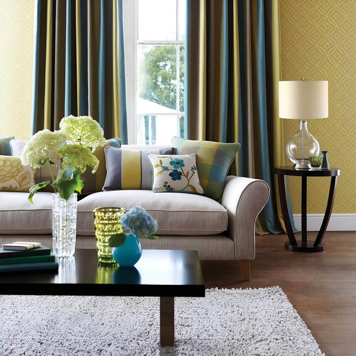 Clear glass base table lamp with a white drum shade on a side table in a colourful living room.