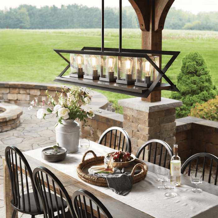 Linear rectangular outdoor chandelier with exposed bulbs hanging above a farmhouse-style patio dining table under a covered porch.