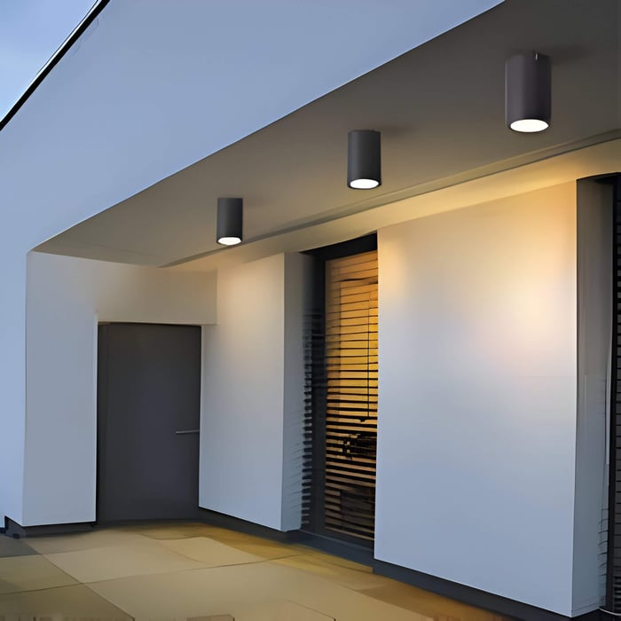 Modern exterior with three cylindrical outdoor downlights mounted under a soffit, casting warm pools of light by a door and window.