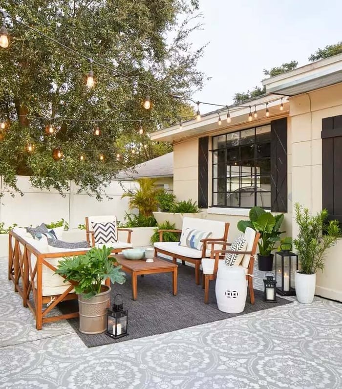 Outdoor string lights strung overhead above a stylish patio seating area with patterned tiles, potted plants, and lanterns.