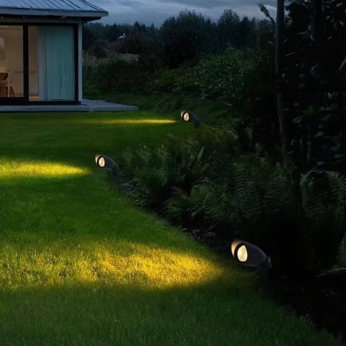 Garden spike spotlights casting warm pools of light across a lawn at dusk.