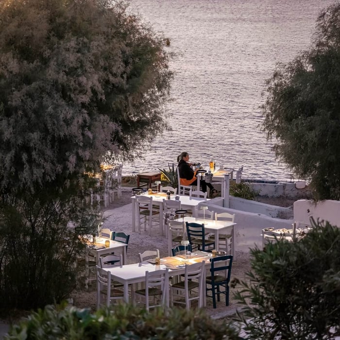 Small glowing table lamps illuminating seaside dining tables at dusk.
