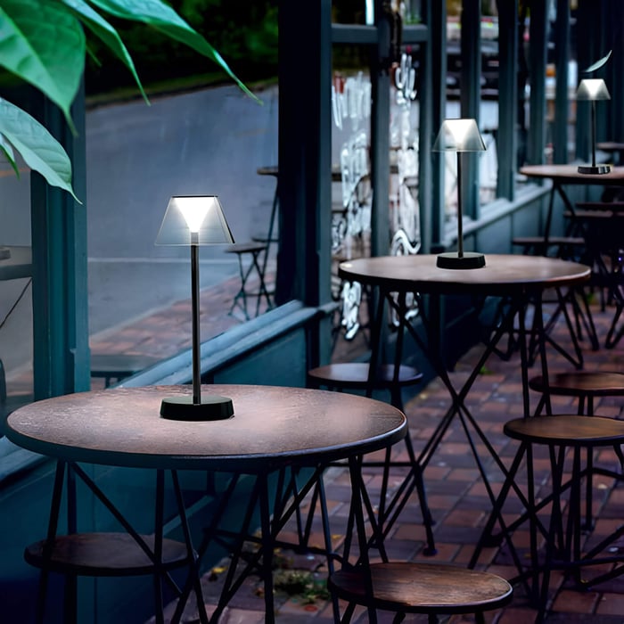 Warm patio dinner scene with glowing pleated Outdoor Table Lamps and string lights in a garden at night.