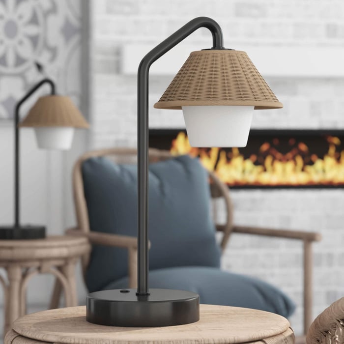 Black Outdoor Table Lamps with rattan cone shade and opal diffuser on patio side table, cozy seating and fireplace in background.