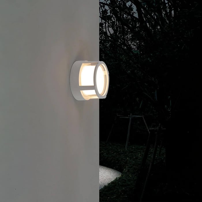 Minimalist exterior wall with two small cone-shaped outdoor wall lights casting warm pools of light under tree shadows.