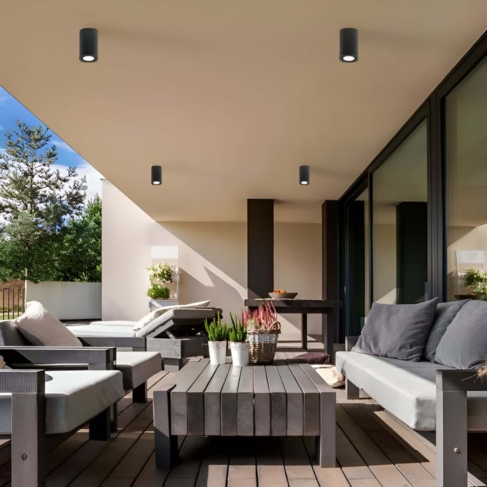 Covered patio with four ceiling-mounted outdoor downlights illuminating a lounge area with gray seating, table, and garden view.