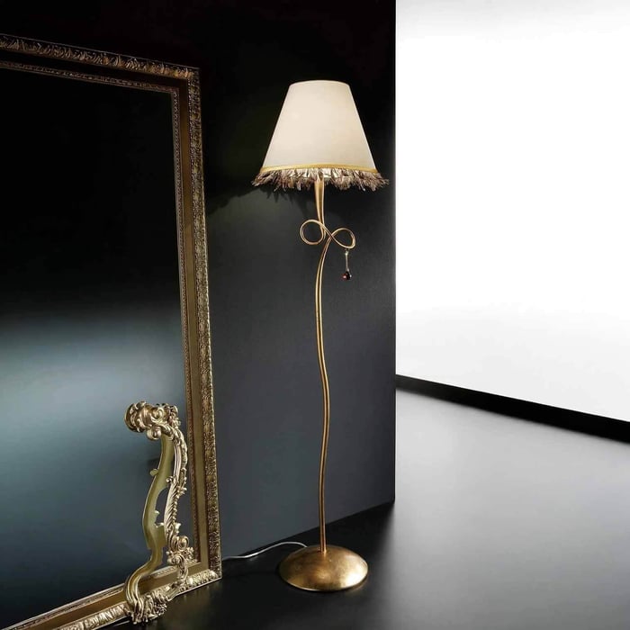 Ornate gold floor lamp with a fabric shade and decorative bow beside a large vintage-style mirror.