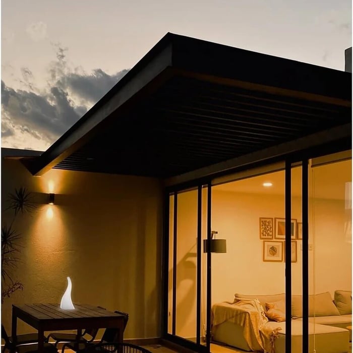 Modern patio at dusk with warm interior glow and a white flame-shaped Outdoor Table Lamps on a small wood dining table beside sliding glass doors.
