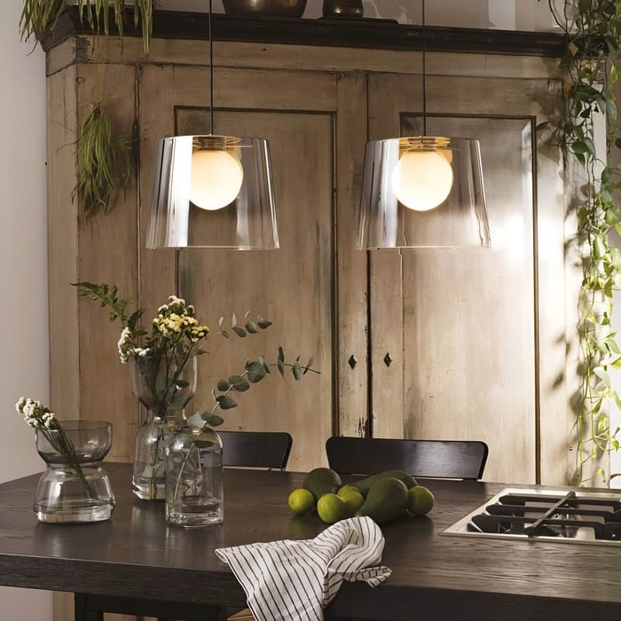 Rustic kitchen setup with glass pendant lights, fresh greenery, and dark wooden table with limes and a striped cloth.