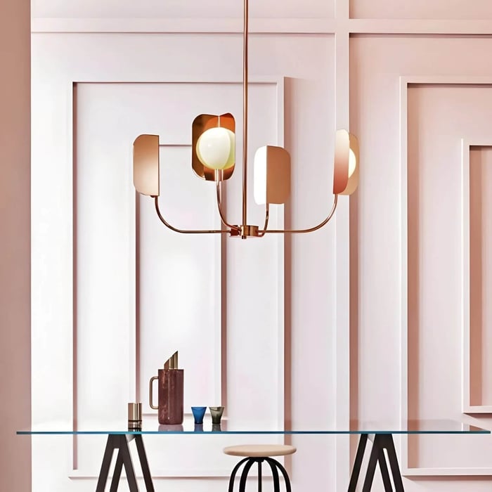 Minimal copper chandelier with petal-shaped shades and frosted globes hanging above a glass table against a geometric white wall backdrop.