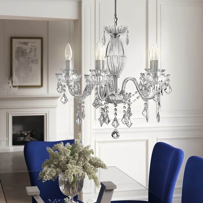 Elegant dining room with a classic crystal chandelier hanging above a glass table, blue upholstered chairs, and a vase of white flowers as the centerpiece.