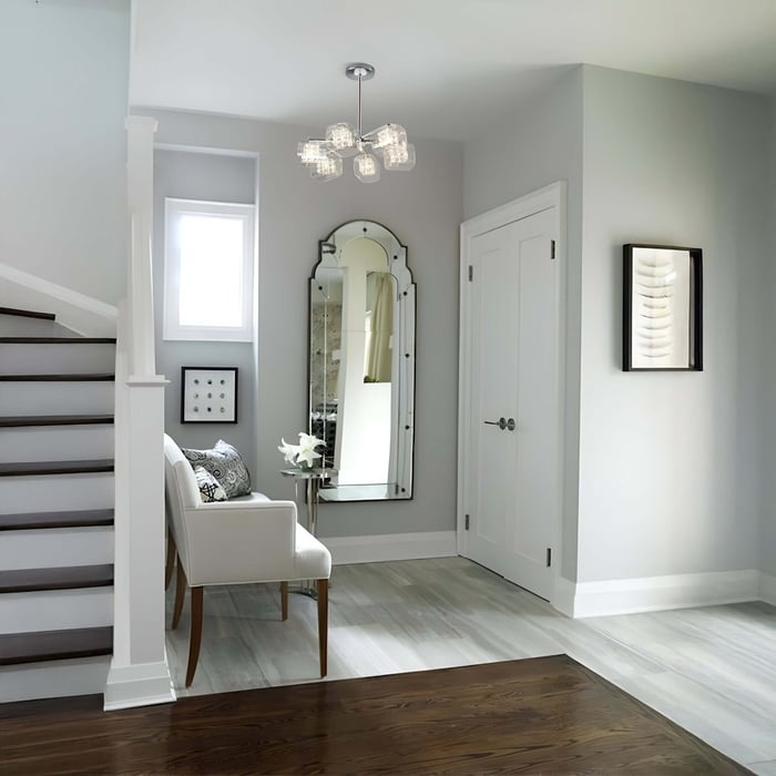 Clustered glass chandelier lighting a modern entryway with a mirror, white bench, and staircase.