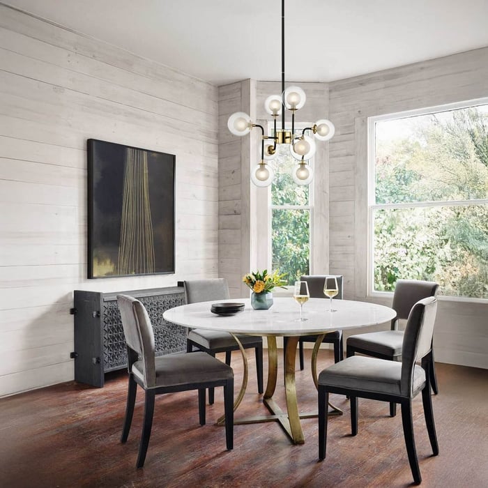 Modern brass chandelier with globe bulbs hanging above a round marble dining table.