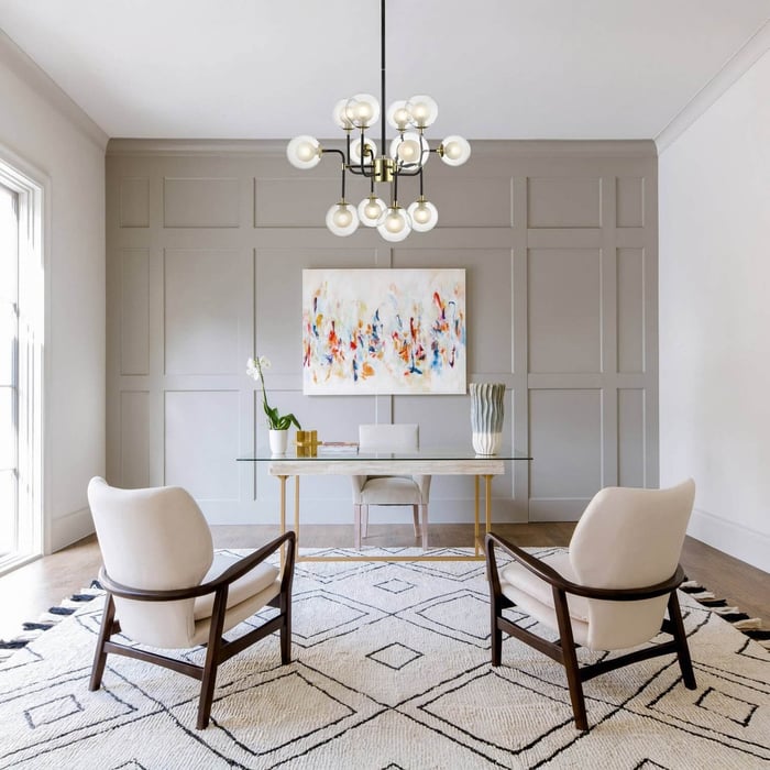 Modern chandelier with globe bulbs hanging above a glass desk in a neutral-toned office with patterned rug.