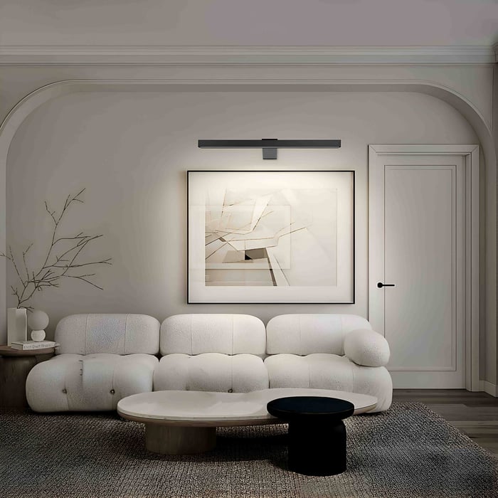 Matte black picture light illuminating a large abstract artwork above a cream bouclé sofa in a minimalist living room with arched wall.