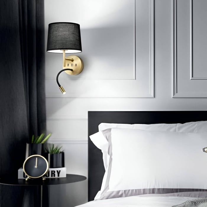 Modern wall sconce with a black shade and brass mount, featuring a reading light arm, ideal for bedside use.