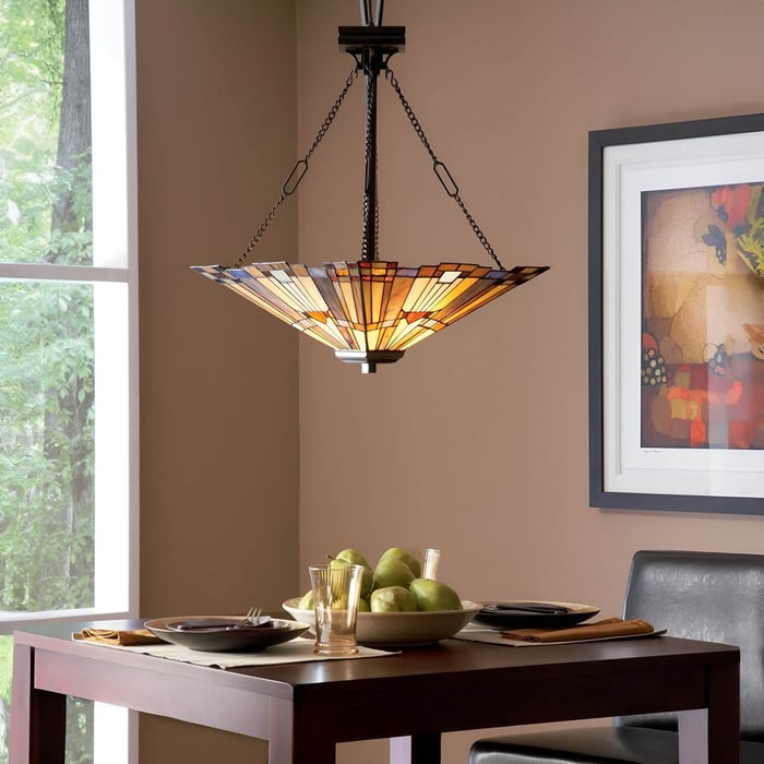 Upside-down pyramid stained glass pendant lamp above a dark wood dining table with place settings and fruit