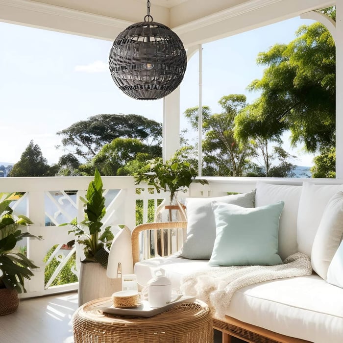 Sunny veranda with a large black rattan globe pendant light above a white outdoor sofa.