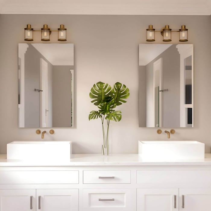 Double vanity with white cabinets, two mirrors, and three-light industrial-style fixtures with brass finishes above each mirror.