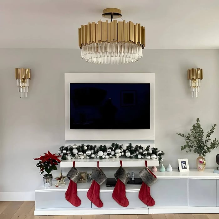Gold-and-crystal drum chandelier centred above a wall-mounted TV, paired with matching wall sconces in a modern living room.