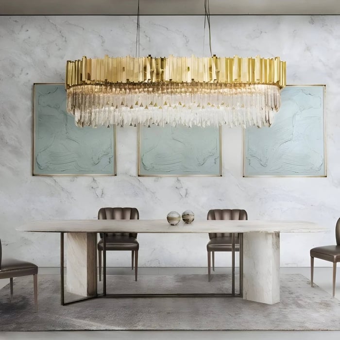 Oval gold and crystal fringe chandelier hanging above a marble dining table in a luxury dining room with framed wall art.