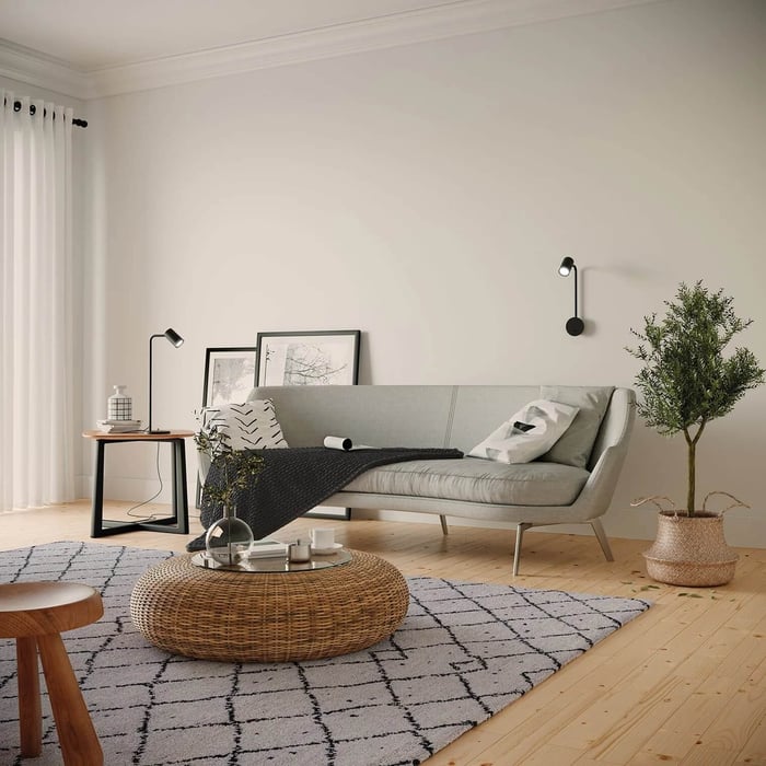 Bright minimalist living room with a grey sofa, woven coffee table, and a small black table lamp on a side table.