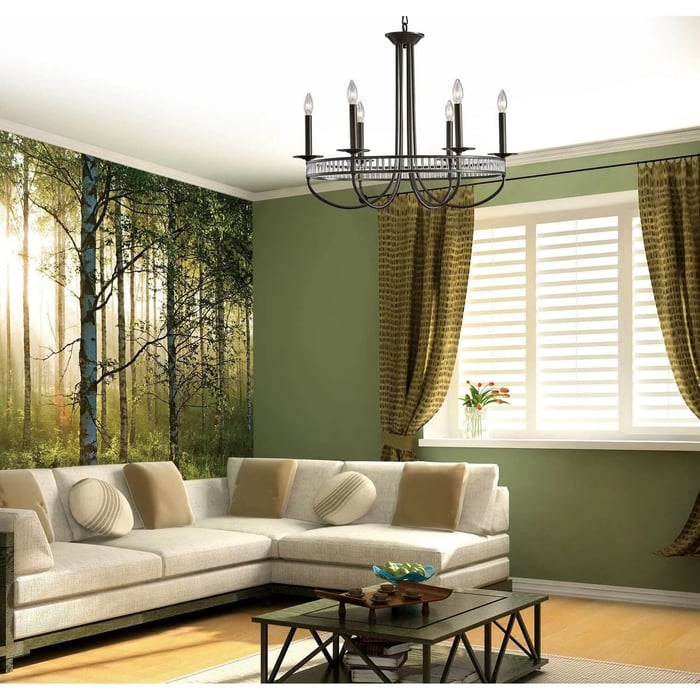 Traditional black metal chandelier with candle-style bulbs hanging above a neutral living room with an L-shaped sofa and green accent walls.