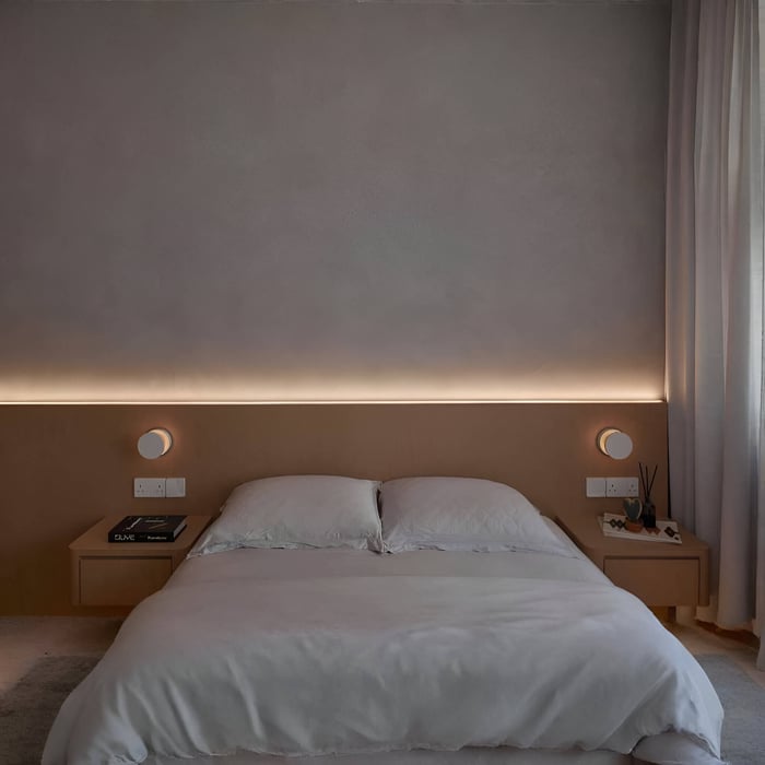 Minimal bedroom with a soft LED strip glow behind the headboard, paired with simple bedside tables and wall-mounted reading lights.