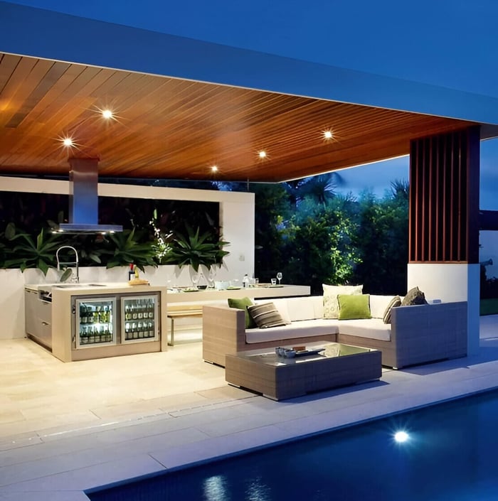 Recessed downlights in a timber ceiling over an outdoor kitchen and lounge area by a swimming pool at dusk.