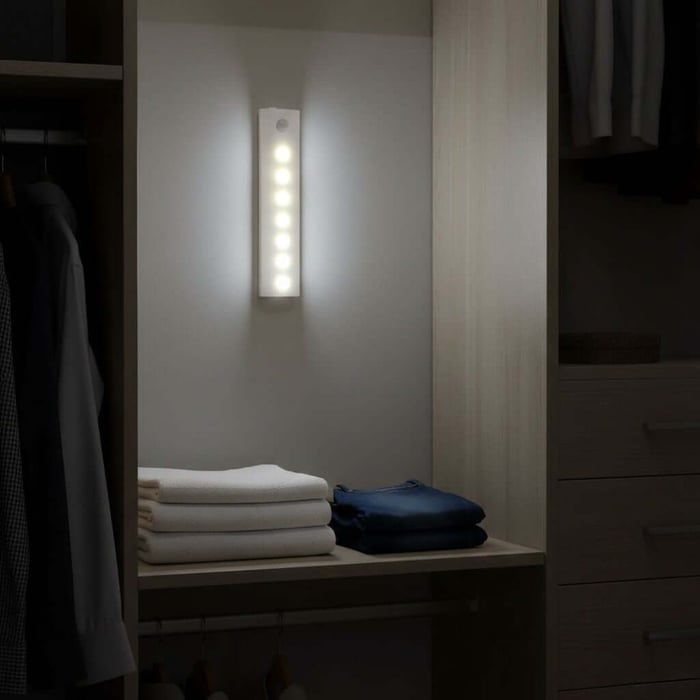 Vertical LED closet light mounted on a wall, illuminating shelves with folded towels and clothes inside a dim wardrobe.