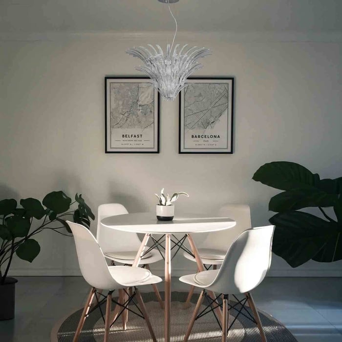 White sculptural chandelier above a small dining table in a minimalist room with framed prints.
