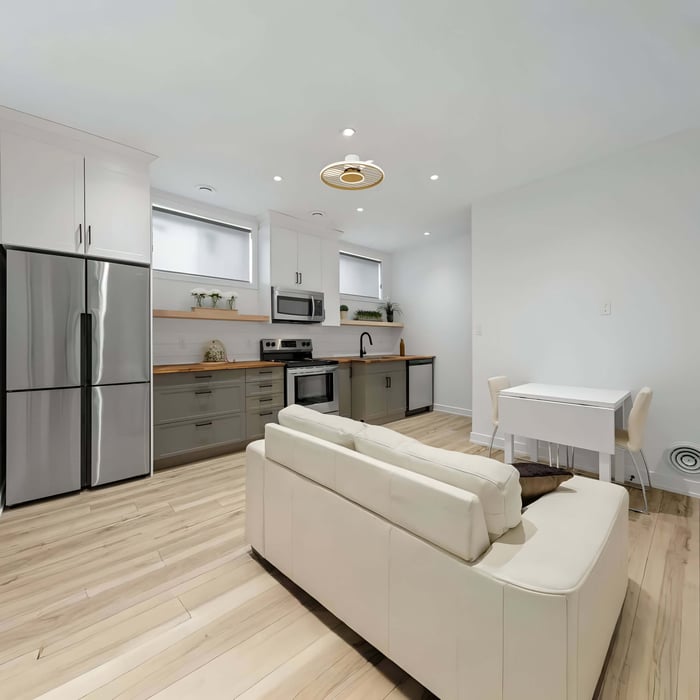 Bright open-plan kitchen and living area with white cabinets, light wood floors, recessed ceiling lights, and a flush-mount ceiling fan light above the room.