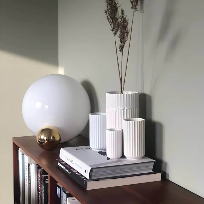 Large white globe table lamp with a brass accent on a wooden shelf with books and white vases.