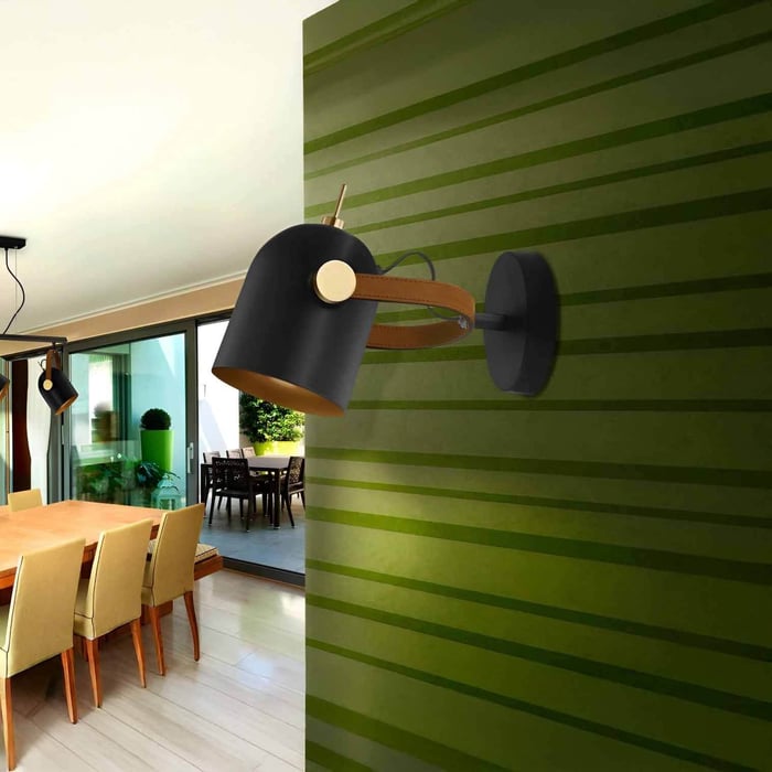 Black adjustable wall spotlight on a green striped feature wall overlooking a dining area, adding directional accent light.