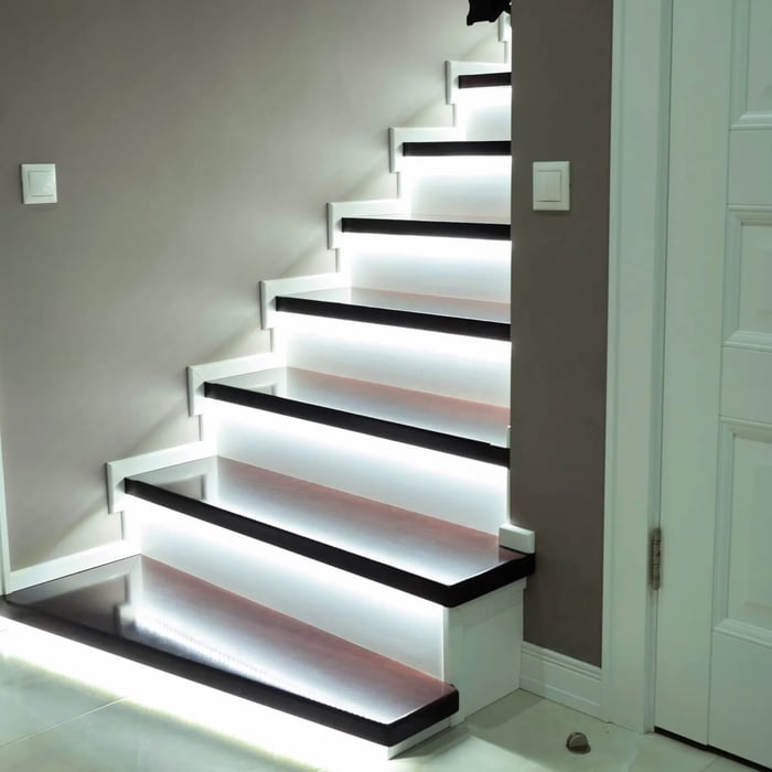 Indoor staircase with bright LED strip lighting under each step, creating clean, glare-free guidance lighting along the stair treads.