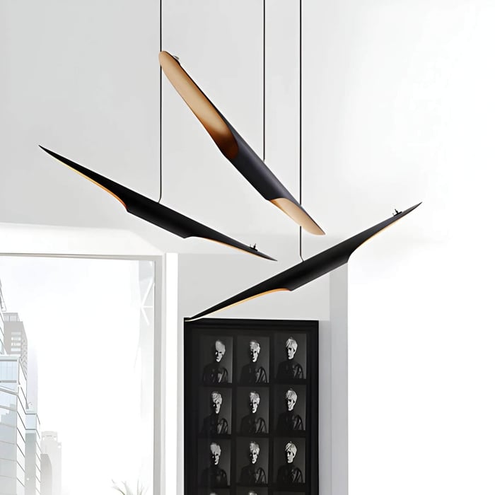 Three sleek black linear pendant lights with warm gold interiors hanging at different angles in a modern, bright room.