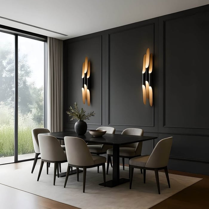 Pair of gold and black sculptural wall sconces on dark paneled walls in a contemporary dining room with cream upholstered chairs.