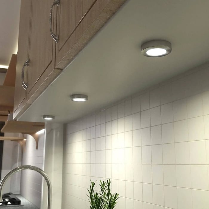 Round under-cabinet puck lights casting even light across a tiled kitchen wall and counter.