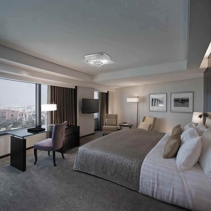 Spacious modern hotel-style bedroom with large windows, a king bed, desk and seating area, and a crystal flush-mount ceiling light.