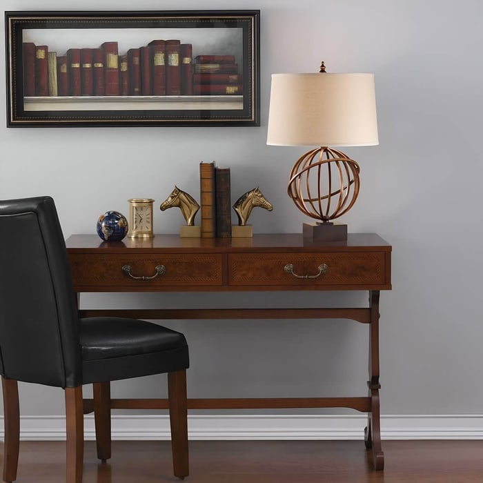 Classic home office with globe-style table lamps, horse bookends, and wall art of books above a wooden desk.