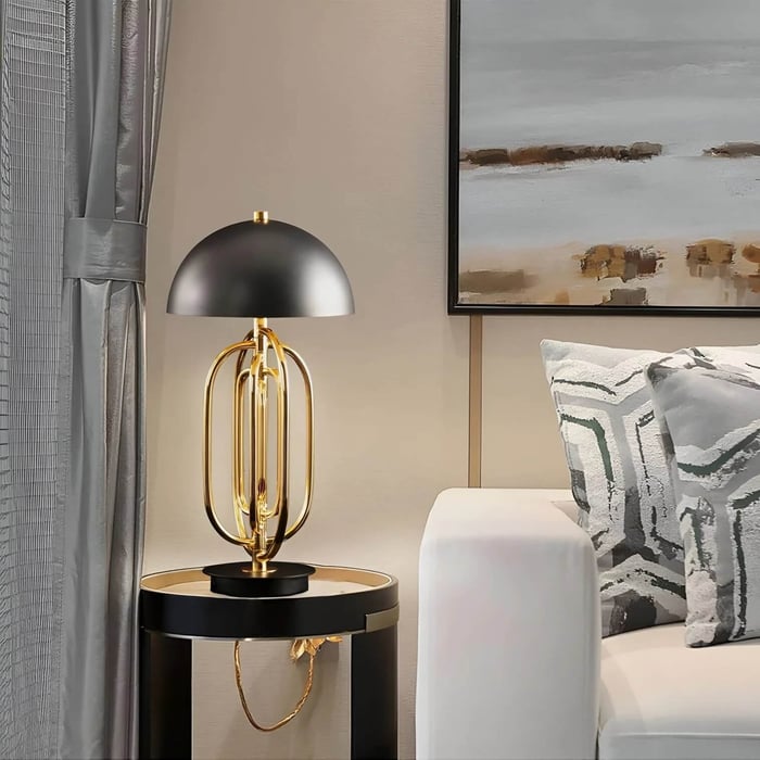 Black and gold designer table lamp with dome shade on a round side table next to a neutral sofa and abstract artwork.