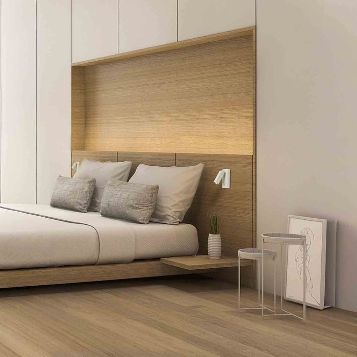 Minimalist bedroom with a recessed wood headboard wall, soft ambient glow, and slim bedside spotlights for reading.