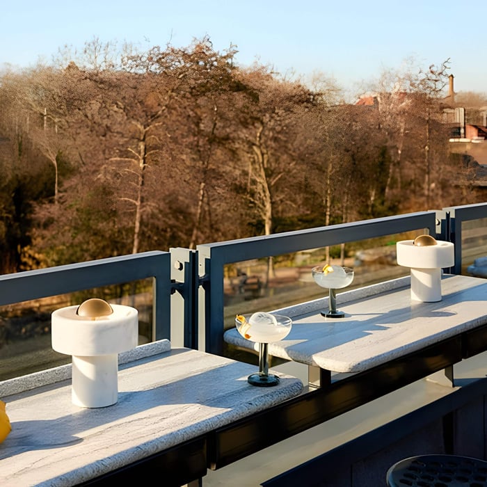 Round white marble portable table lamps on a stone balcony railing, paired with cocktails at golden hour.