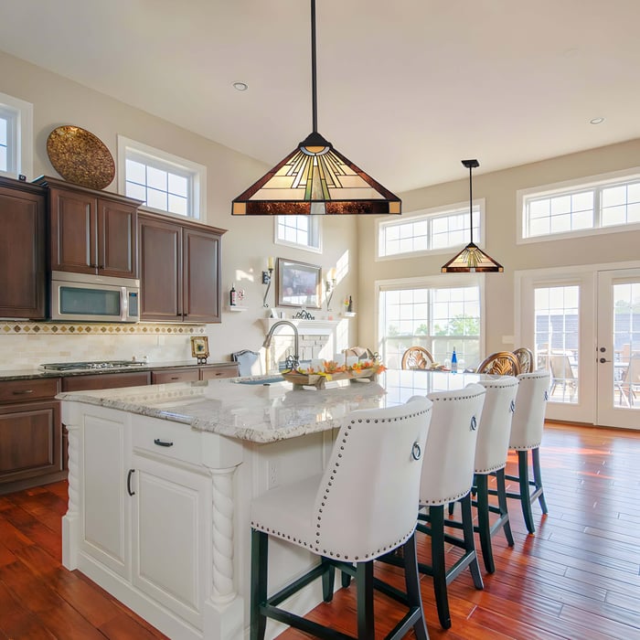 Bright kitchen with two geometric Tiffany pendants over a marble island, flanked by white walls and dark cabinetry.