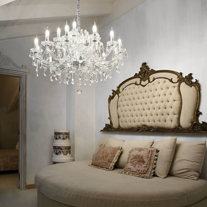 Classic bedroom with tufted headboard, ornate frame, and a large crystal chandelier casting an elegant glow.