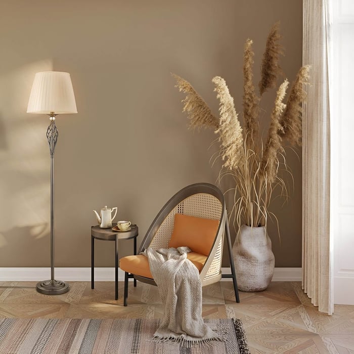 Bronze floor lamp with pleated shade beside a rattan chair in a warm-toned reading nook with pampas grass and textured flooring.