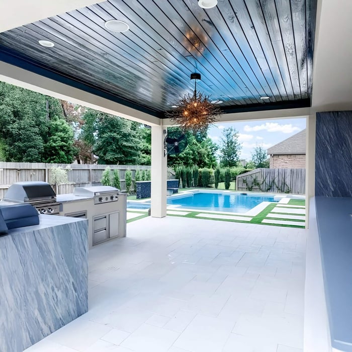 Modern starburst pendant light with multiple rods hangs over a covered poolside kitchen area.
