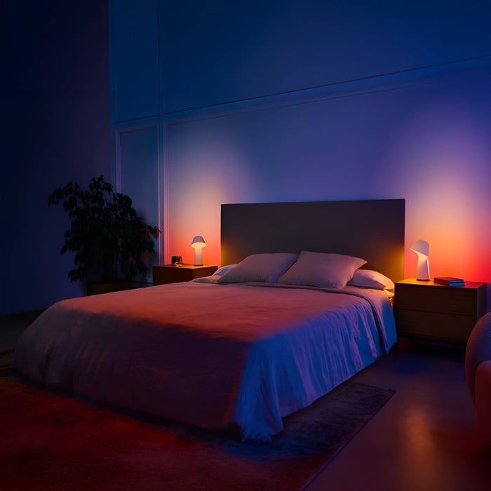 Dark bedroom lit by two small bedside lamps casting colored ambient light in blue, red, and orange tones.