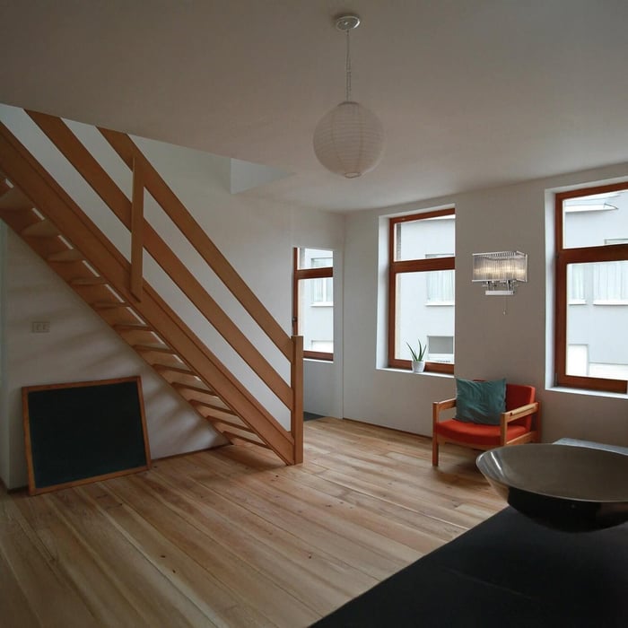 Bright interior with wooden stairs, orange chair, and crystal wall sconce by window.