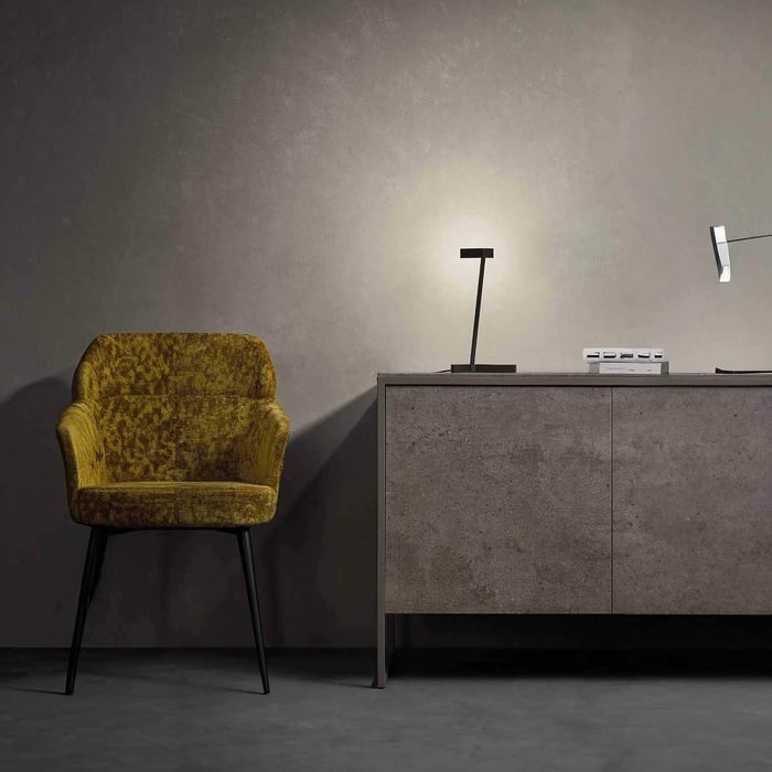 Minimal interior with a yellow accent chair and a slim black table lamp on a grey sideboard against a textured wall.